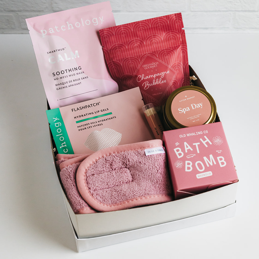 White gift box with bath bomb, candle, face mask, treats, and pink spa headband