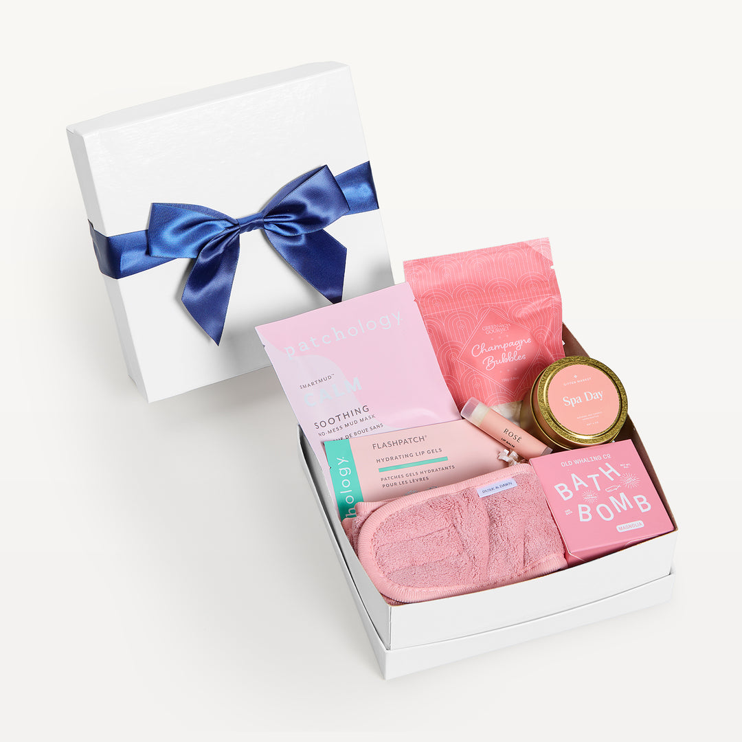 Rosy Outlook, white shallow box open in front, bow-tied lid behind. Patchology mask, Champagne Bubbles pouch, Spa Day candle tin, pink spa headband, Old Whaling bath bomb, Flashpatch lip gels. Giften Market.