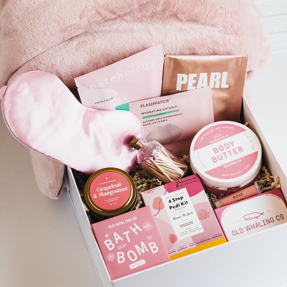 White gift box with pink eye mask, bath bomb, body butter, candle, and spa treats