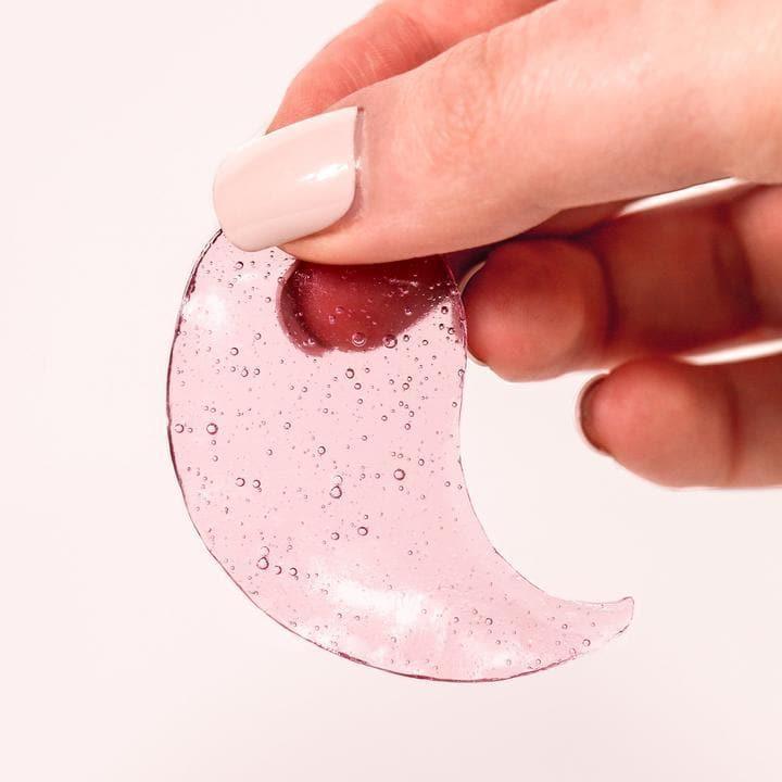 Hand holding a pink gel under-eye patch with small bubbles on a light background