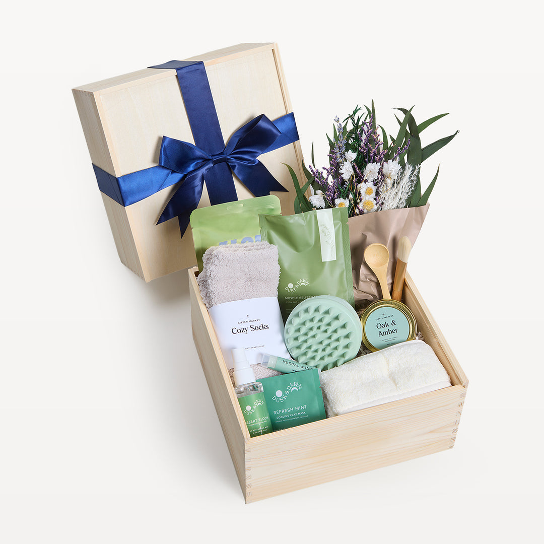 Soothing Sanctuary Classic crate open in front, bow-tied lid propped behind. Wildflower bouquet, Cozy Socks, Oak &amp; Amber candle tin, green scalp massager, Refresh Mint clay mask, spray. Giften Market.