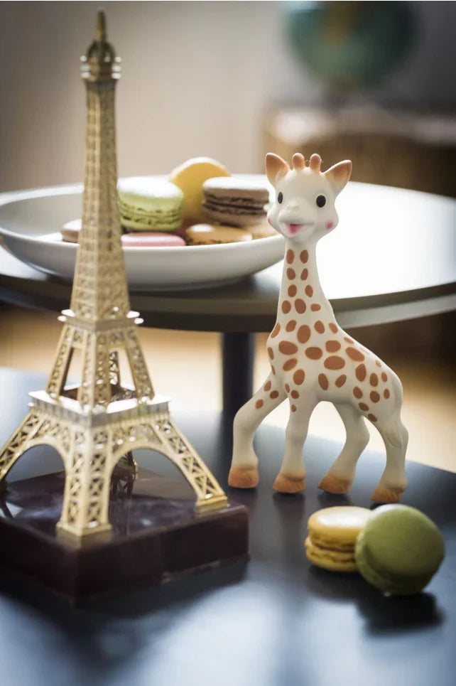 Baby giraffe teether with Eiffel Tower figurine and assorted macarons on a modern table