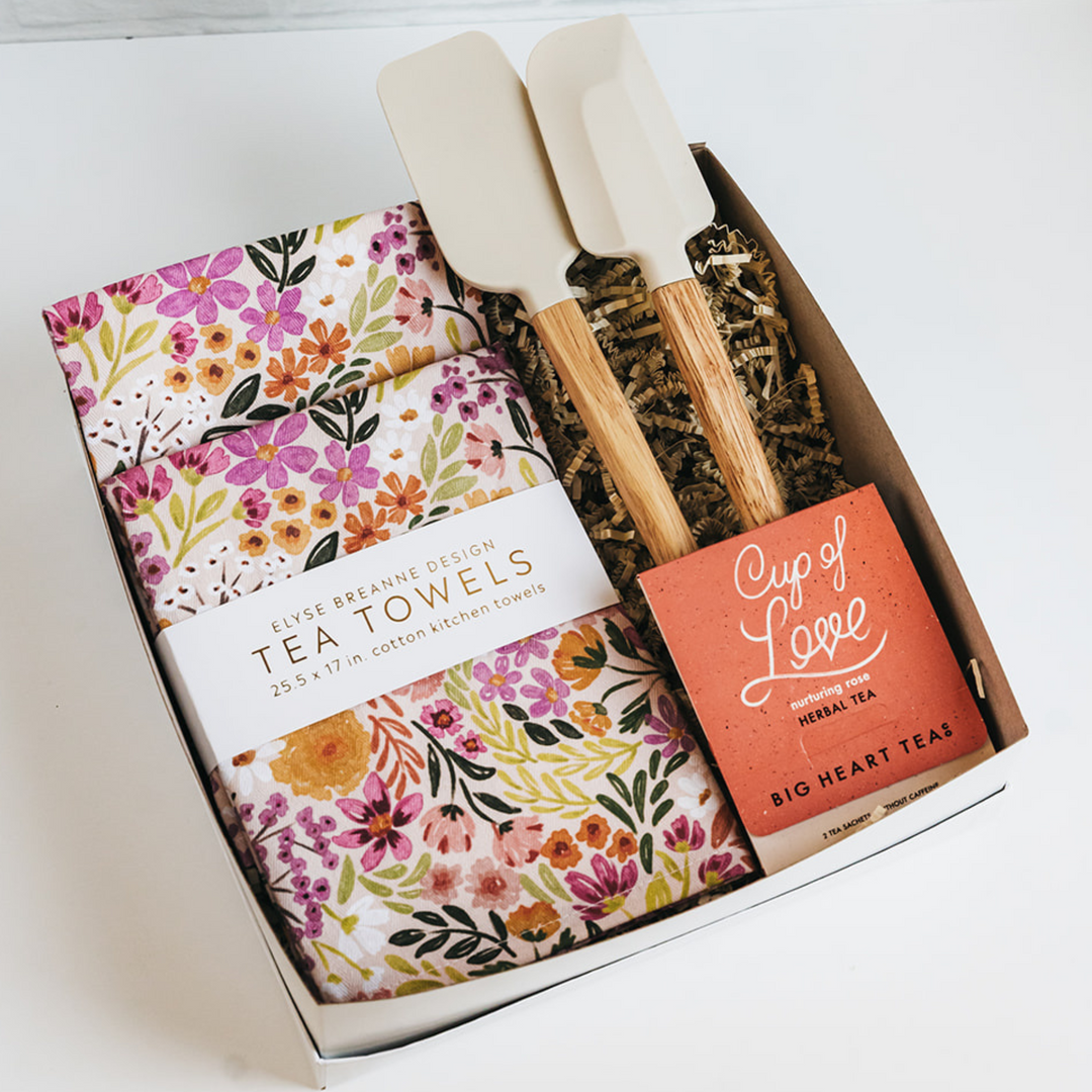 Box containing tea towels, spatulas, and a tea bag on a white background