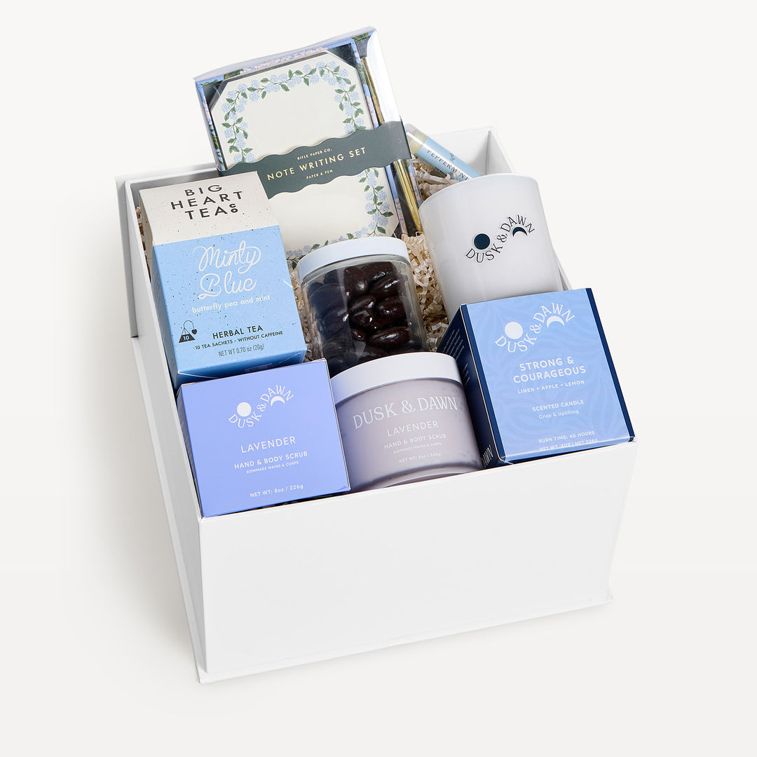 Strong &amp; Courageous Deluxe, white gift box, lid off. Big Heart Teas Minty Blue, note writing set, jar of chocolate-covered almonds, cream candle, Lavender hand and body scrub, Strong &amp; Courageous candle box, Lavender jar. Giften Market.