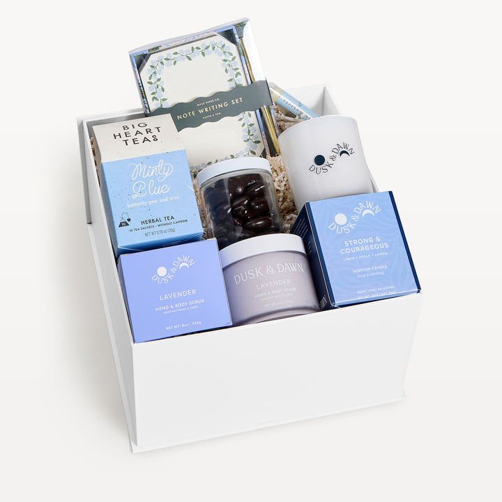 Strong &amp; Courageous Deluxe, white gift box, lid off. Big Heart Teas Minty Blue, note writing set, jar of chocolate-covered almonds, cream candle, Lavender hand and body scrub, Strong &amp; Courageous candle box, Lavender jar. Giften Market.