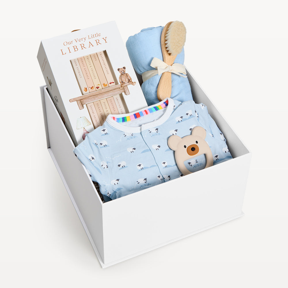 Sweet Beginnings Baa Baa Blue, white gift box, lid off. Blue sheep-print zip onesie, Our Very Little Library, blue swaddle, wooden brush, bear teether. Giften Market.