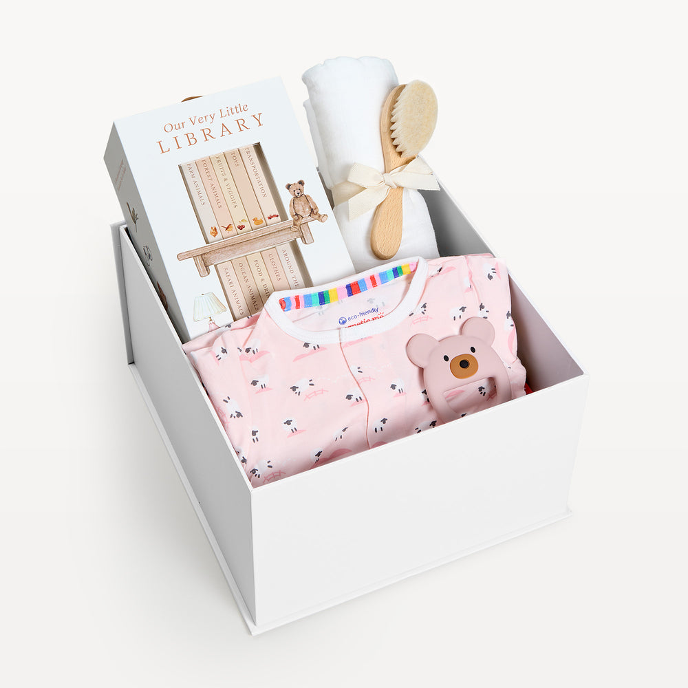 Sweet Beginnings Baa Baa Pink, white gift box, lid off. Pink sheep-print zip onesie, Our Very Little Library, white swaddle, wooden brush, bear teether. Giften Market.