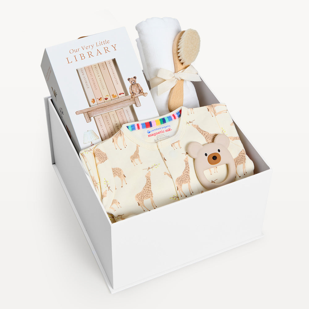 Sweet Beginnings Jolie Giraffe, white gift box, lid off. Cream giraffe-print zip onesie, Our Very Little Library, white swaddle, wooden brush, bear teether. Giften Market.
