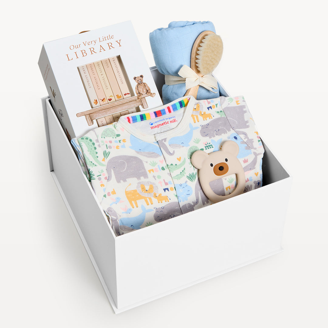 Sweet Beginnings Little Lovin, white gift box, lid off. Safari-animal print zip onesie, Our Very Little Library, blue swaddle, wooden brush, bear teether. Giften Market.