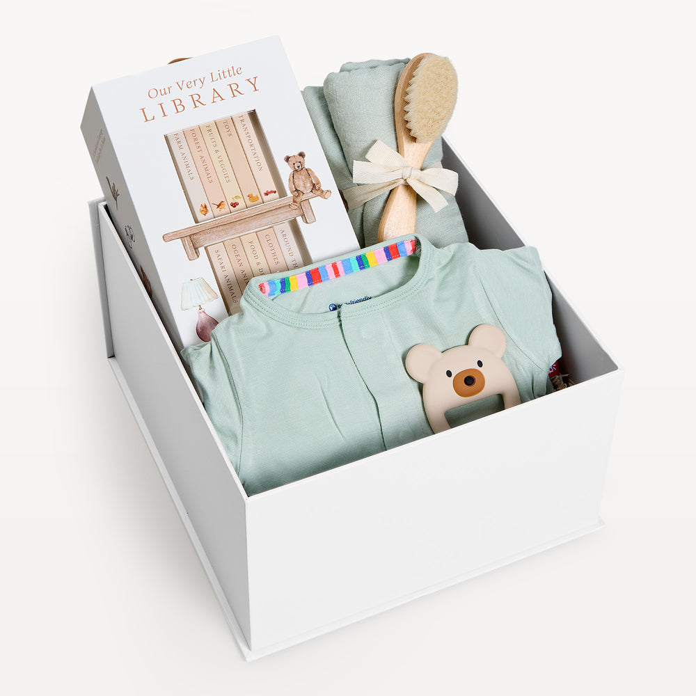 Sweet Beginnings Sea Foam, white gift box, lid off. Sage zip onesie, Our Very Little Library, sage swaddle, wooden brush, bear teether. Giften Market.