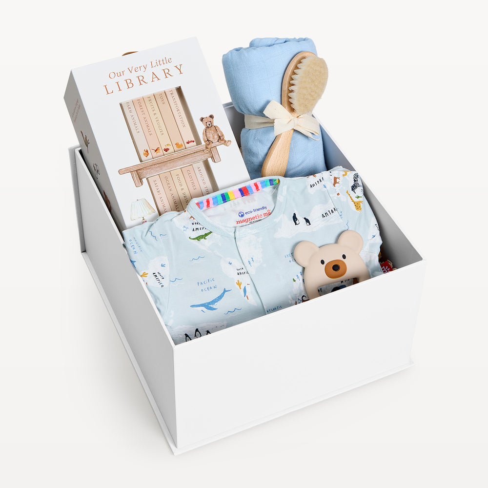Sweet Beginnings Sea the World, white gift box, lid off. Pale blue world-map print zip onesie, Our Very Little Library, blue swaddle, wooden brush, bear teether. Giften Market.