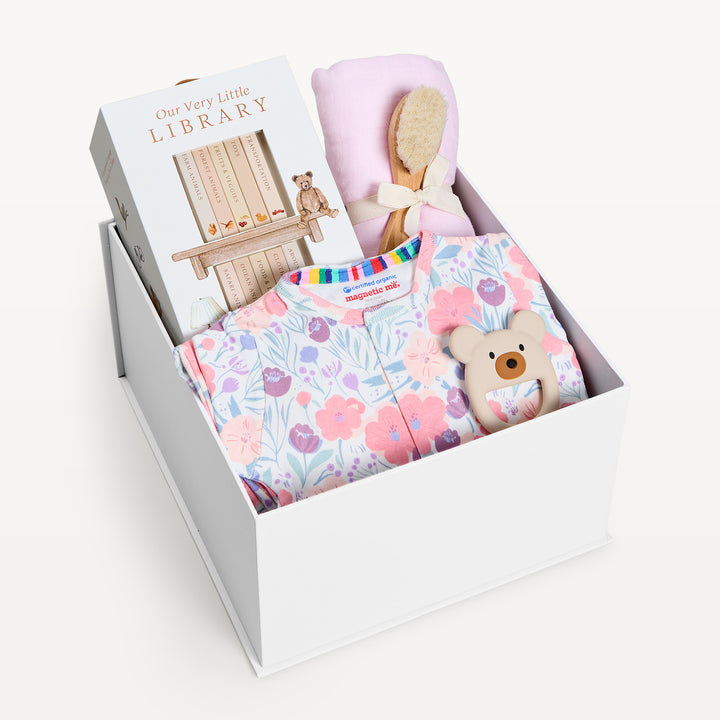 Sweet Beginnings Whistledon, white gift box, lid off. Pink and lilac floral zip onesie, Our Very Little Library, pink swaddle, wooden brush, bear teether. Giften Market.