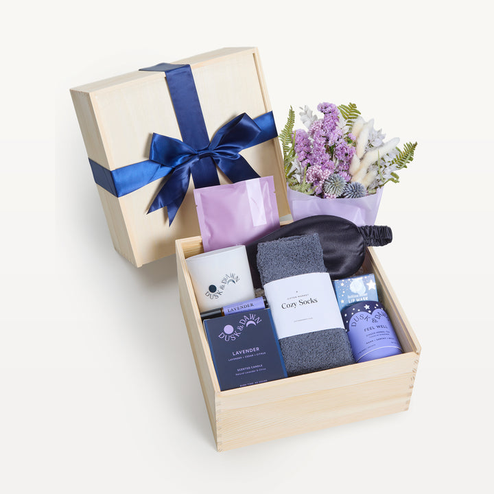 Sweet Dreams crate open in front, bow-tied lid behind. Lavender dried bouquet, black sleep mask, gray Cozy Socks, Dusk &amp; Dawn Lavender candle, Feel Well tea, lilac packets. Giften Market.