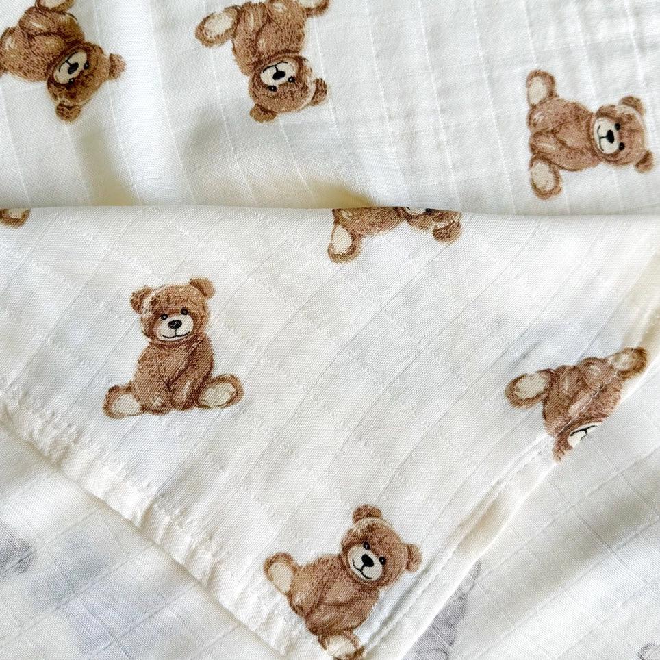 White bamboo muslin swaddle blanket with brown teddy bear print, folded neatly