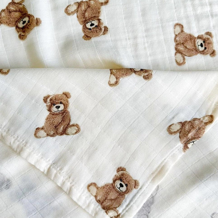 White bamboo muslin swaddle blanket with brown teddy bear print, folded neatly