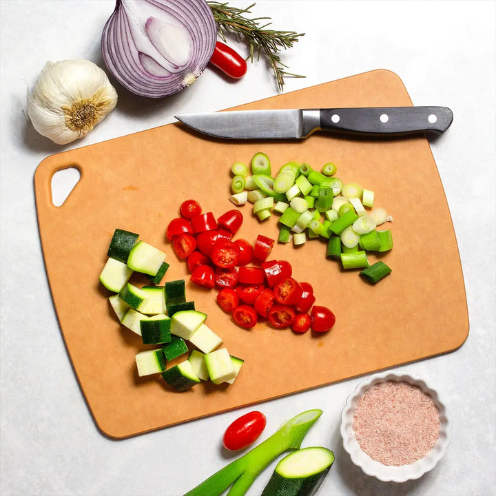Wood fiber cutting board with chef’s knife, chopped vegetables, garlic, and seasoning