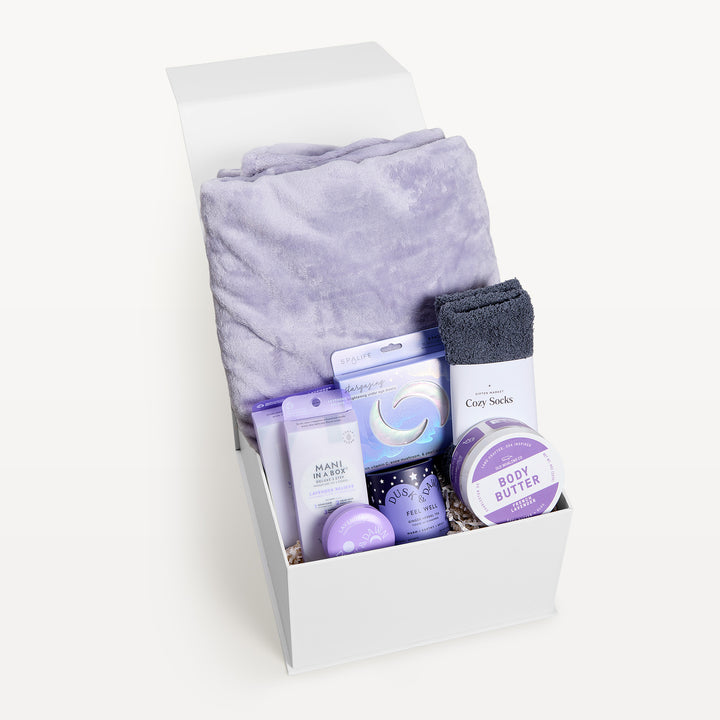 Virtual Hug Deluxe Classic Lavender, white gift box, lid open. Lilac faux-fur throw, Mani in a Box, SpaLife Stargazing mask, gray Cozy Socks, Lavender body butter, Feel Well tea, Dusk &amp; Dawn tin. Giften Market.