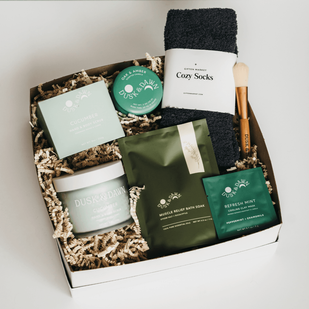 Wellness Ritual Gift Box open with green Dusk & Dawn spa items, cucumber mask, bath soak, candle tin, mask brush and charcoal cozy socks