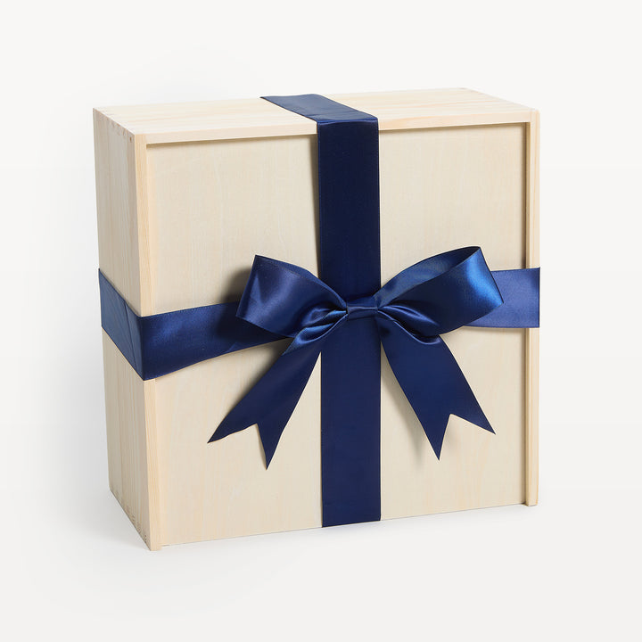 Empty 10x10x6 pine gift crate, lid closed, navy satin ribbon tied in a bow across the top. Packaging only, no contents. Giften Market.