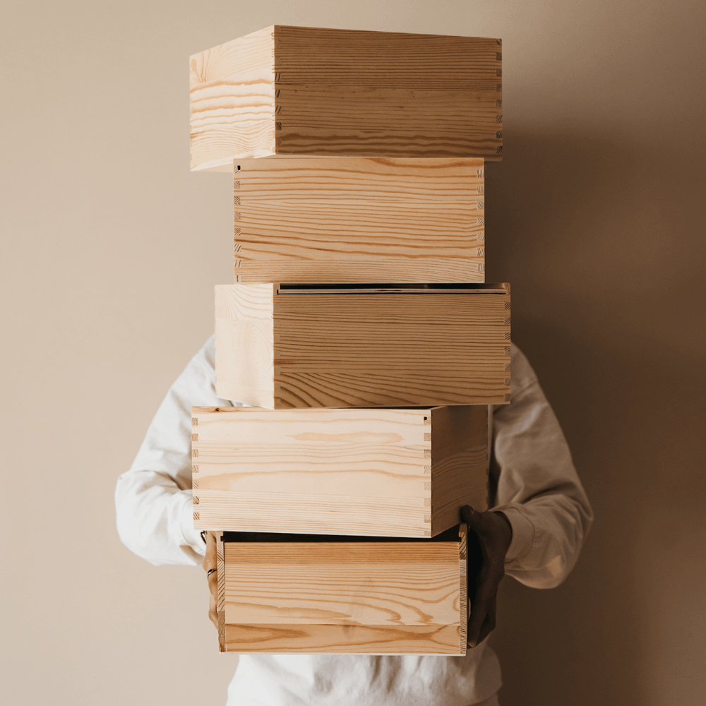 Person holding a stack of empty wooden gift crates against a neutral background